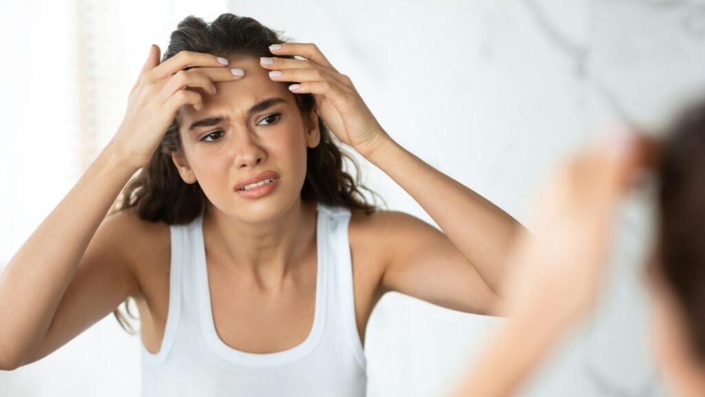 Sad Woman With Acne Issue Squeezing Pimple On Forehead Indoor