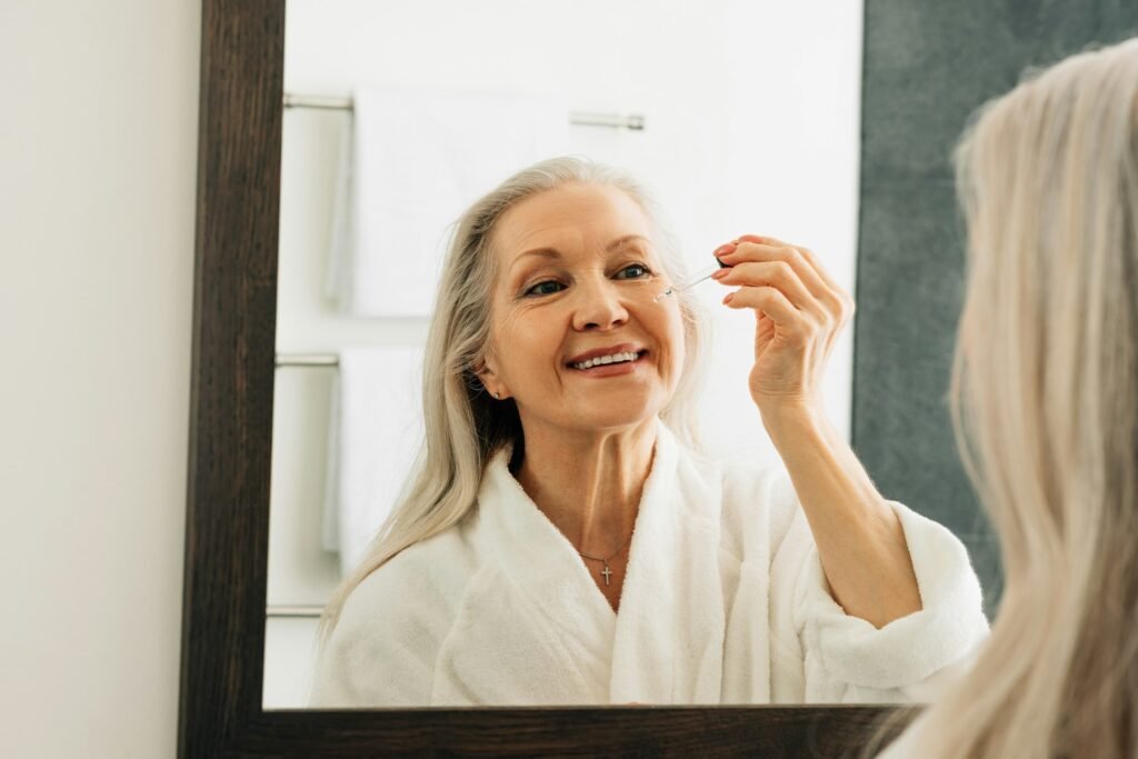 Smiling aged female applying the liquid facial treatment on face